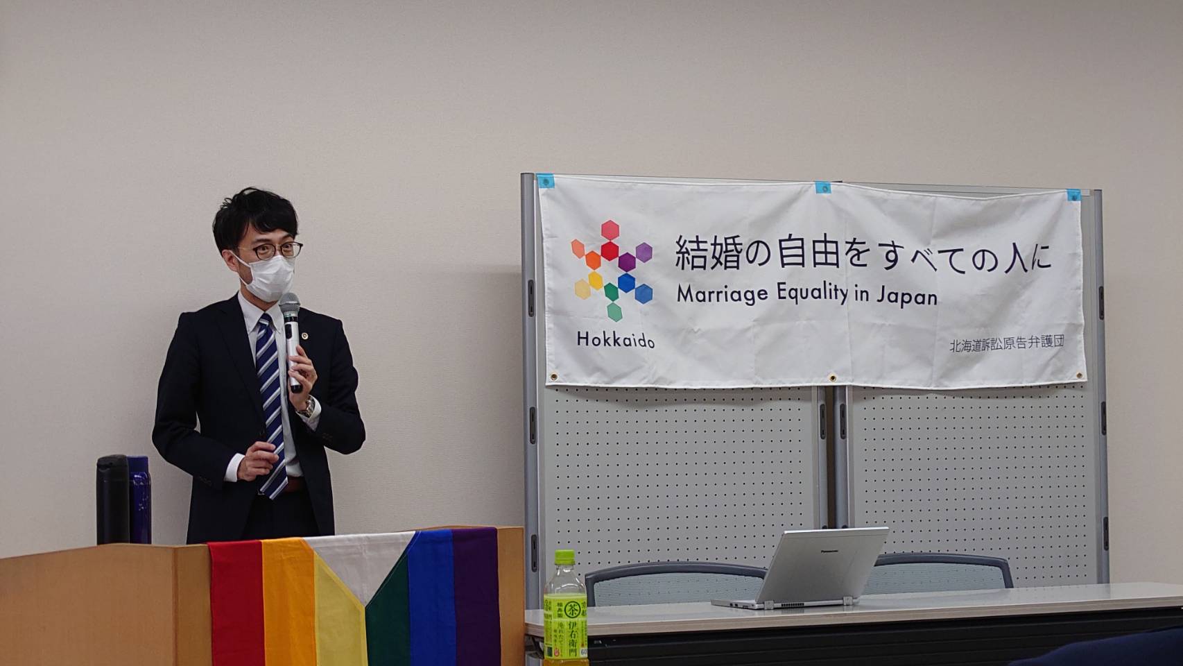 綱森史泰弁護士が、マイクを持ちながら、2022年11月30日に下されたと今日判決について話をしている。「結婚の自由をすべての人に Marriage Equality in Japan　北海道訴訟原告弁護団」と書かれた旗が掲げられている。