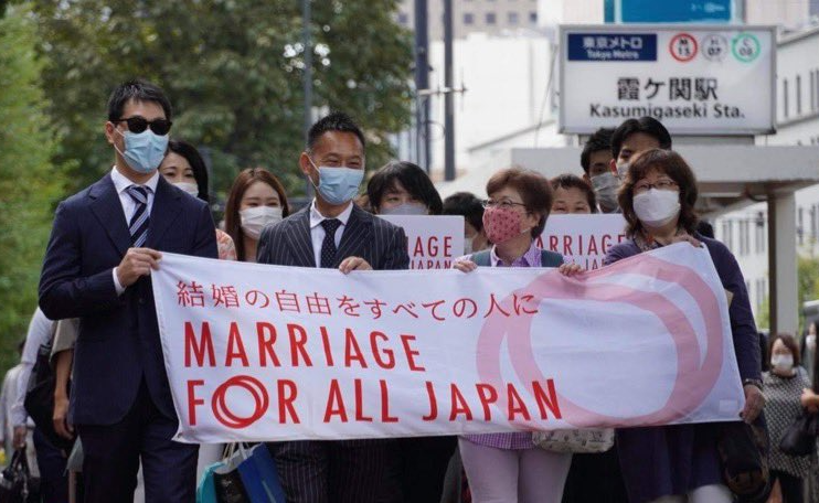 画像。結婚の自由をすべての人に訴訟、東京第一次訴訟入廷行動の様子。原告たちを先頭 にして、笑顔を見せながら東京地方裁判所前の沿道を歩いている。