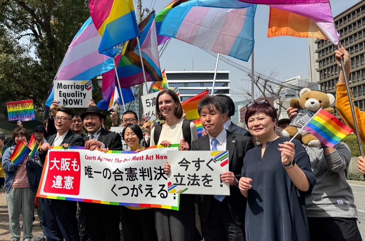 大阪高裁判決の後、裁判所の前で、唯一の合憲判決くつがえると書かれた横断幕を掲げる原告と弁護団