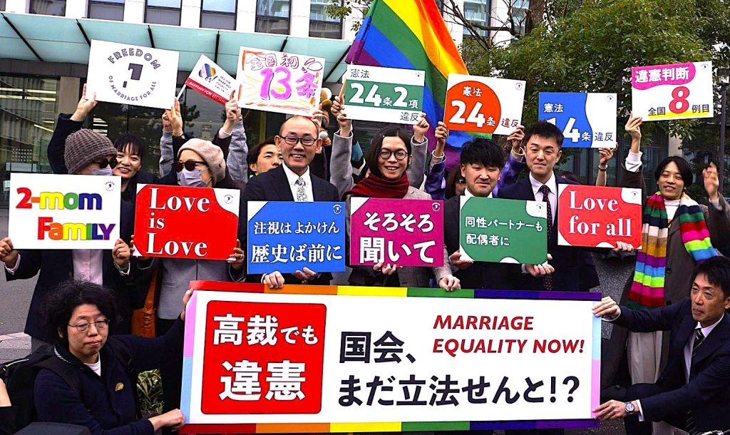 12月13日、福岡高裁前。同性婚ができないことは憲法13条、14条1項、24条2項に違反するとの判決がなされました！ そのことを、裁判所前から伝えてる写真です。笑顔がたくさん見えます。 九州訴訟の原告、弁護団が横断幕やボードを持っています。 大きなメッセージは、 高裁でも違憲 国会、まだ立法せんと！？ 原告さんのメッセージは左から、 ・2-mom Family (母2人家族) ・Love is Love 原告ココさんとミコさんから。 ・注視はよかけん　歴史ば前に　こうぞうさん ・そろそろ聞いて　ゆうたさん ・同性パートナーも配偶者に　こうすけさん ・Love For All まさひろさん 後ろの弁護団のボード　左から ・九州訴訟のロゴマーク(FREEDOM of marriage for all アルファベットの間には九州がデザインされています。) ・全国初13条 (間に見えてるのは、マリフォーの結婚の平等にYESの旗です。) ・憲法24条2項違反 ・憲法24条違反 ・憲法14条違反 ・違憲判断全国8件目