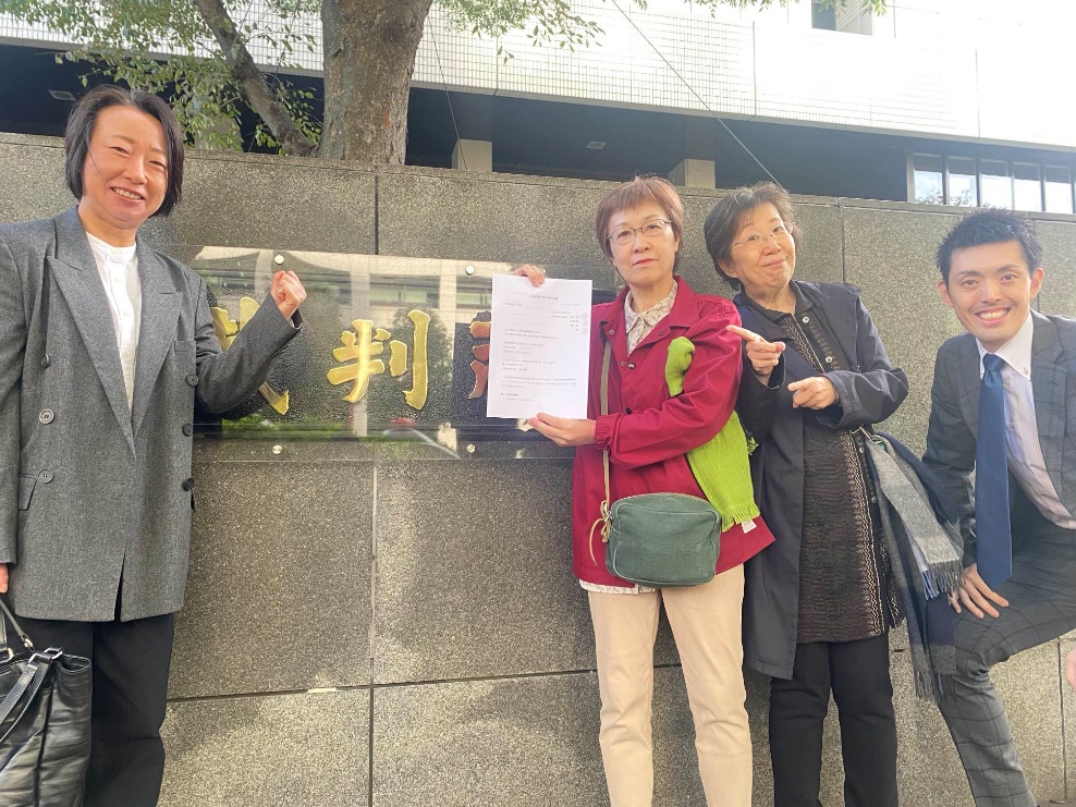 「上告兼上告受理申立書」をもって掲げる「結婚の自由をすべての人に」東京１次訴訟原告の小川葉子さん、それを指さす原告の大江千束さん、その左右に笑顔の上杉崇子弁護士と加藤慶二弁護士の写真（東京高裁の正門前にて）