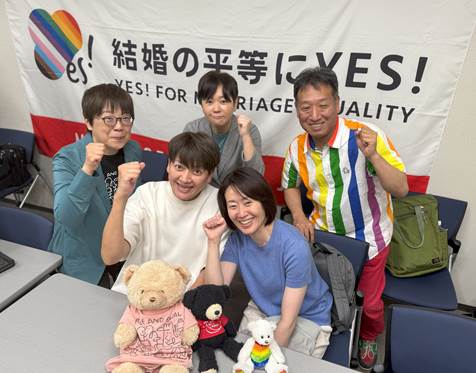 「結婚の平等にYES!」と書かれた横断幕の前で、笑顔でガッツポーズをとる「結婚の自由をすべての人に」東京２次訴訟の原告５人（後列は左から鳩貝さん、河智さん、前列は左から藤井さん、福田さん、山縣さん）。その前にはクマのぬいぐるみ３体が置かれている。