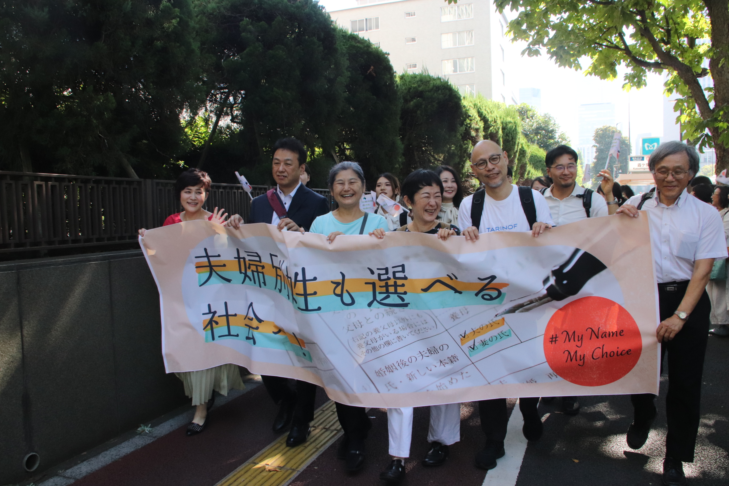 横断幕を掲げて弁護団と原告が入廷行動する様子。笑顔が見られる。
