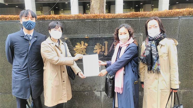 東京地方裁判所の前で控訴状を手にもつ原告小野と原告西川。二人の脇に弁護団員が2名いる。