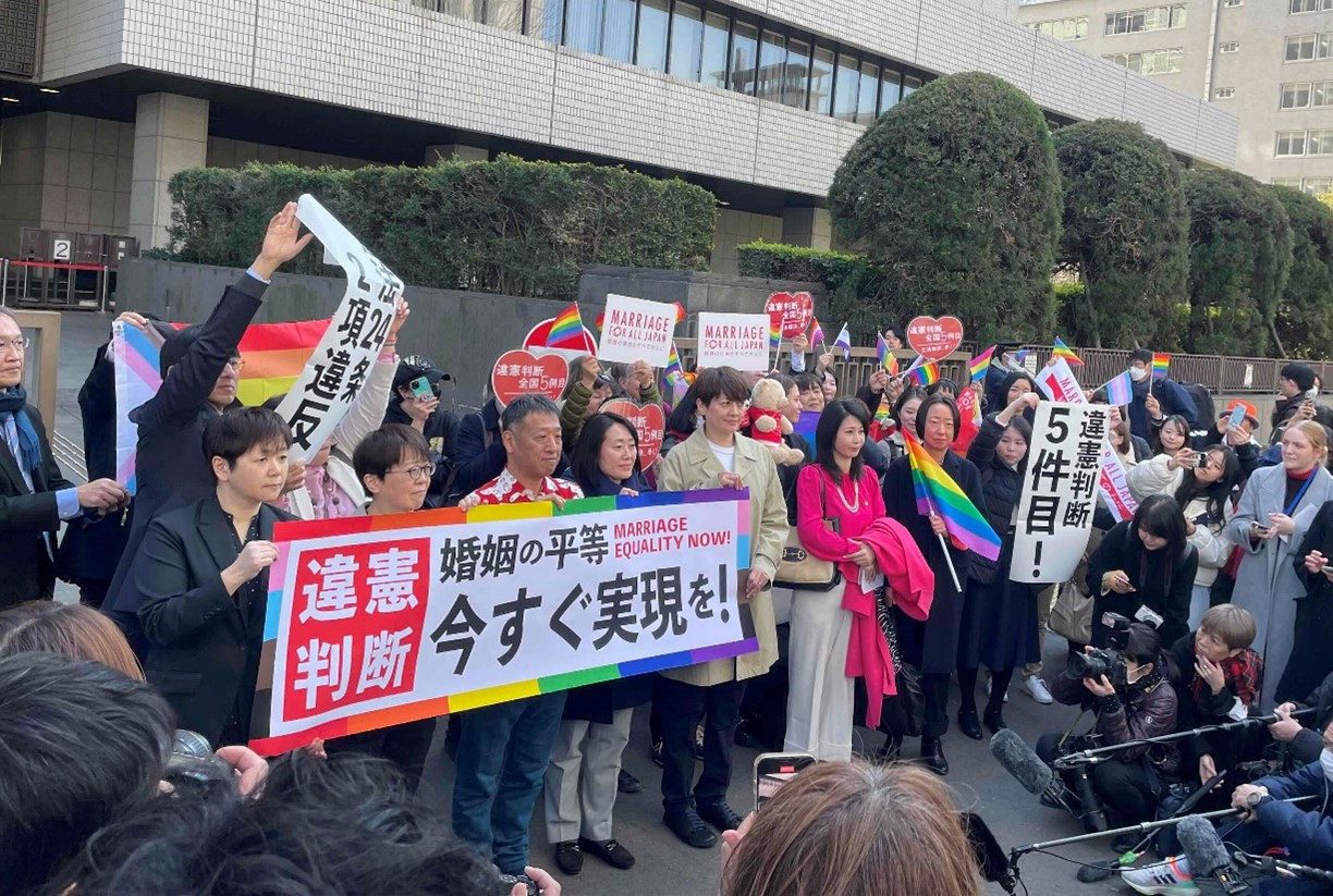 東京地方裁判所前で「違憲判断」と書かれた旗を持つ原告らと弁護団員