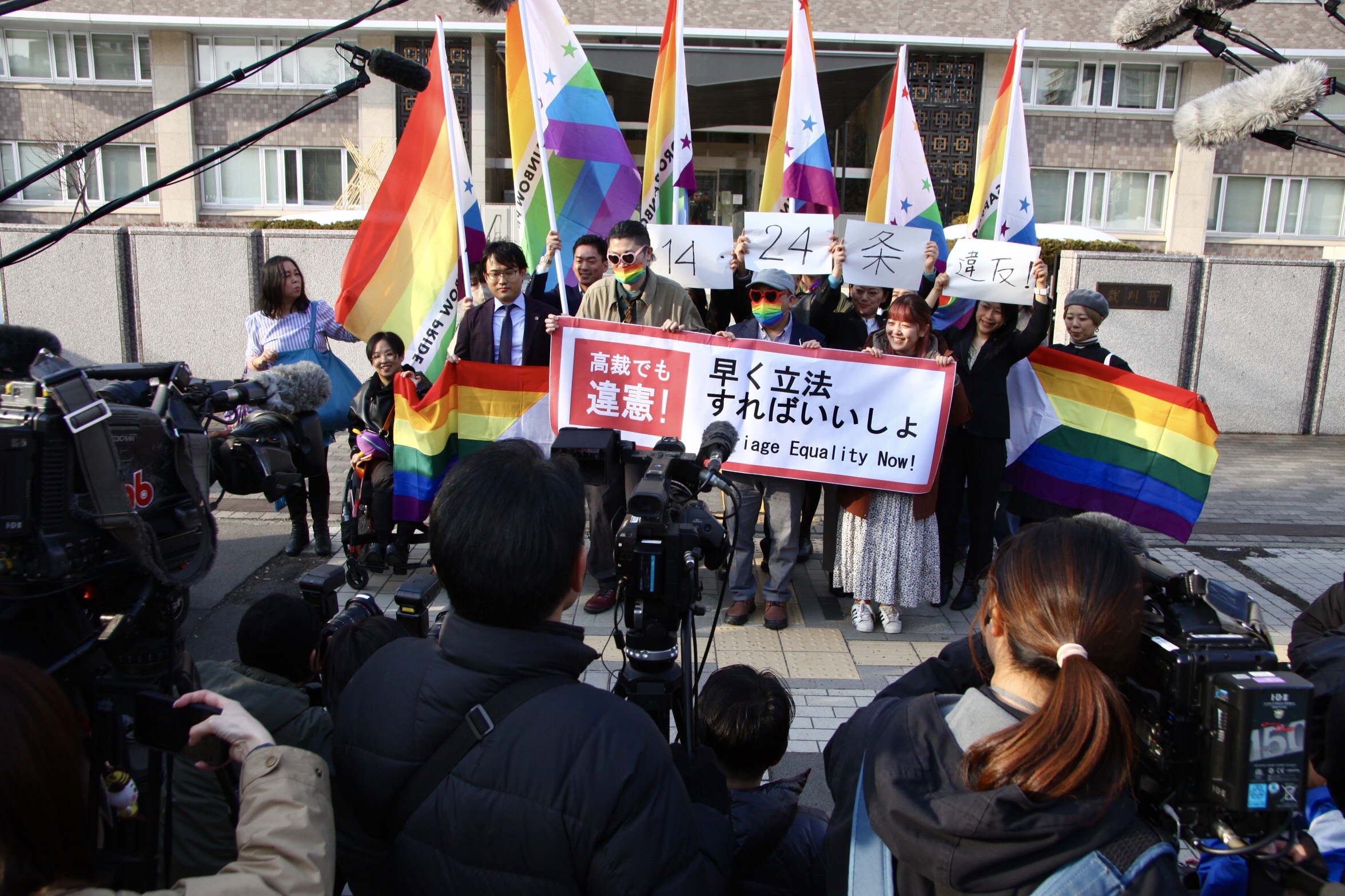 札幌地方裁判所の前で、「結婚の自由をすべての人に」北海道訴訟の原告と弁護団、支援者が、「高裁でも違憲！　早く立法すればいいしょ」と書かれた横断幕やレインボーカラーの旗を掲げている。